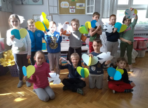 Grupa dzieci stojących w sali, trzyamja w rękach papierowe gołębie i serca w barwach narodowych Ukrainy